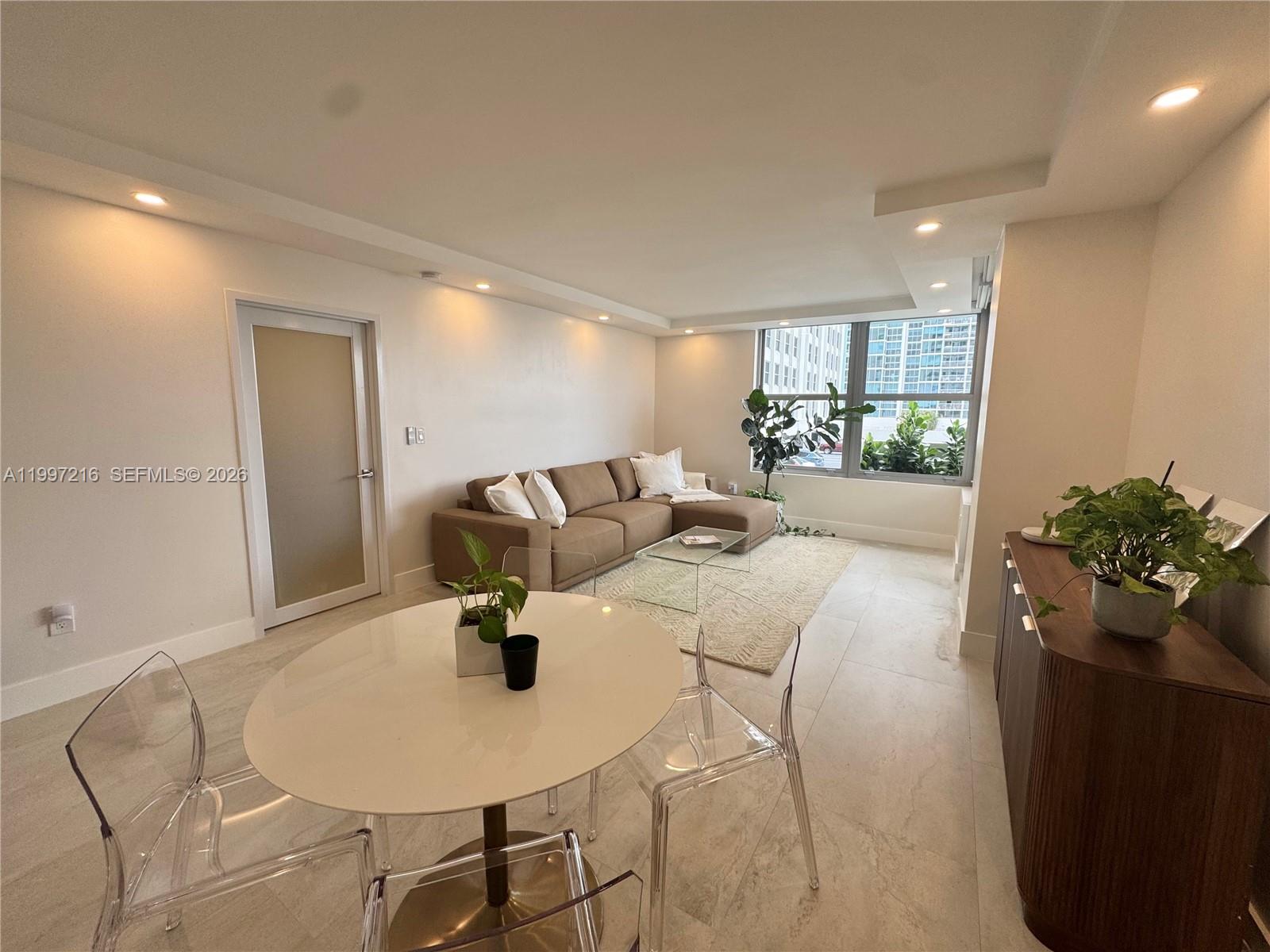 A living and dining area features a sectional sofa, round table, and large windows — 2899 Collins Ave # 424, Miami Beach FL 33140, MIAMI BEACH, FL