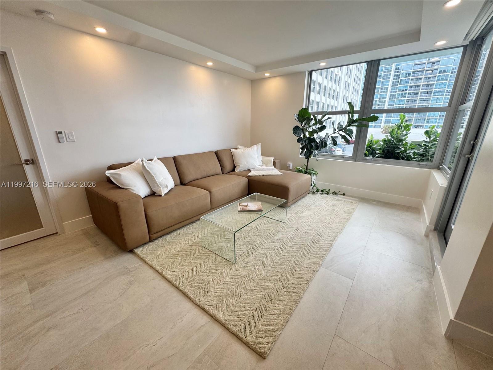 A living room features a brown sectional sofa, glass coffee table, and large window — 2899 Collins Ave # 424, Miami Beach FL 33140, MIAMI BEACH, FL