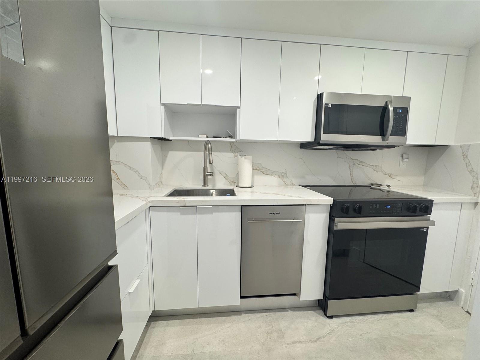 A modern kitchen features white cabinets, stainless steel appliances, and marble-patterned countertops and backsplash — 2899 Collins Ave # 424, Miami Beach FL 33140, MIAMI BEACH, FL