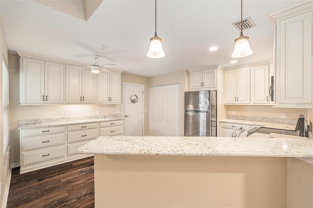 A kitchen features cream-colored cabinets, granite countertops, stainless steel appliances, and dark wood flooring — 21527 WOODSTORK LANE, LUTZ, FL