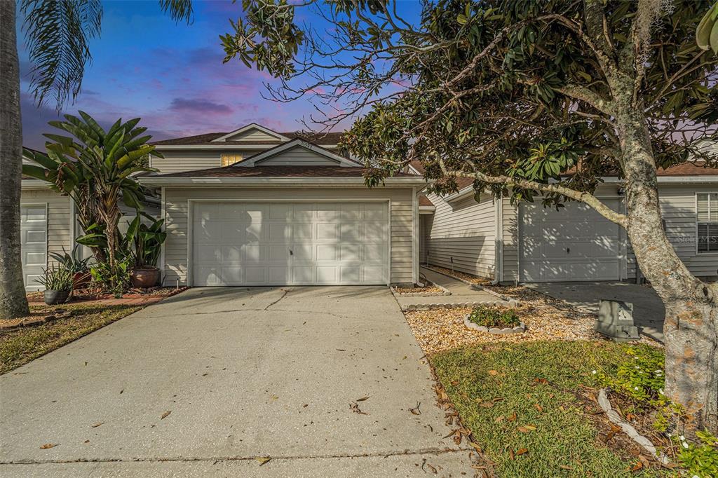 A two-story townhouse with a white garage door, concrete driveway, and surrounding trees — 21527 WOODSTORK LANE, LUTZ, FL