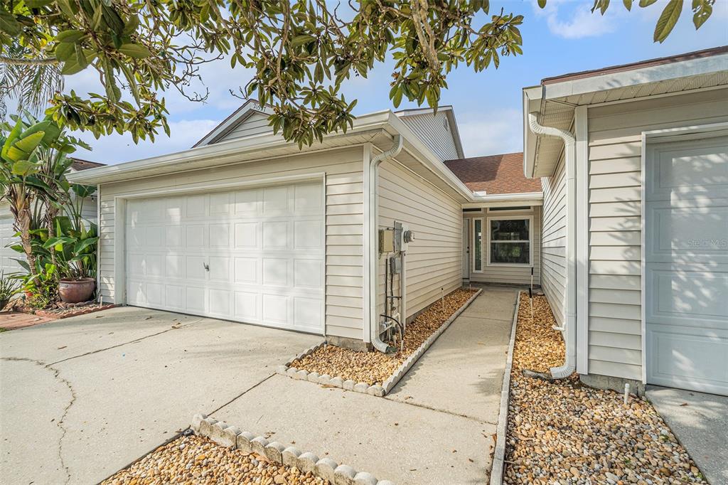 A beige house exterior features a white garage door, a concrete walkway, and gravel landscaping — 21527 WOODSTORK LANE, LUTZ, FL