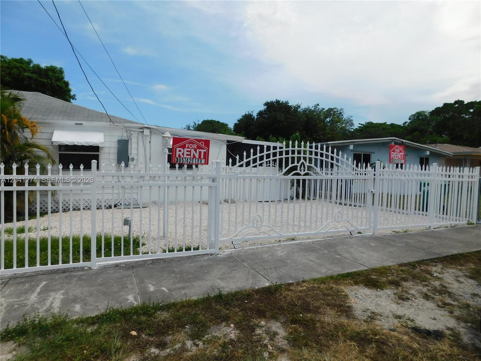 A white metal fence encloses the front yard of two single-story houses for rent — 2230 NW 58th St # B, Miami FL 33142, MIAMI, FL