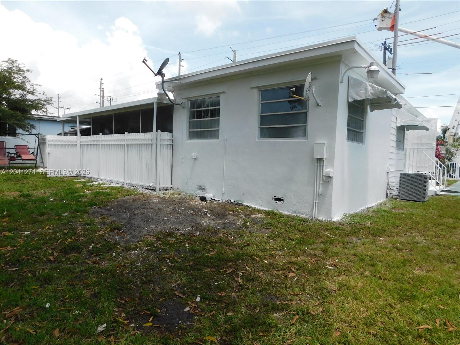 The exterior of a white house features a fenced patio, windows, and an air conditioner — 2230 NW 58th St # B, Miami FL 33142, MIAMI, FL