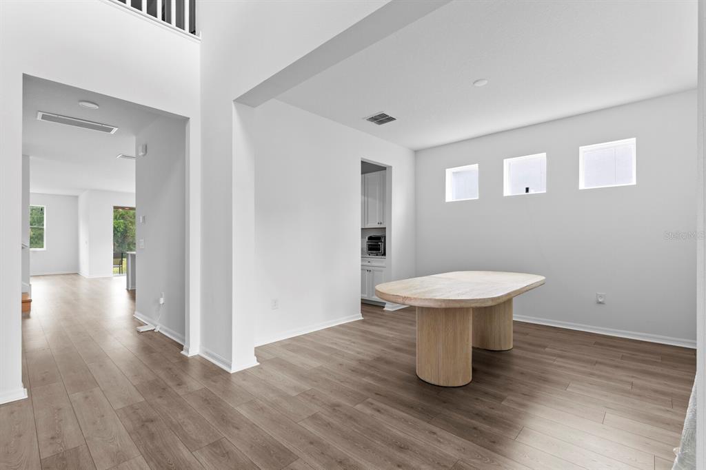 A dining area with light wood flooring, a large oval table, and three high windows — 10742 NEW MORNING DRIVE, TAMPA, FL