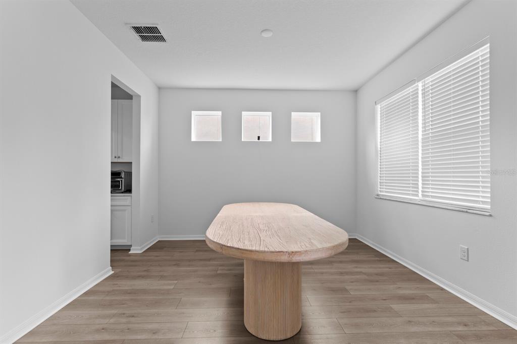 A dining room with light wood flooring, a central pedestal table, and three small square windows — 10742 NEW MORNING DRIVE, TAMPA, FL
