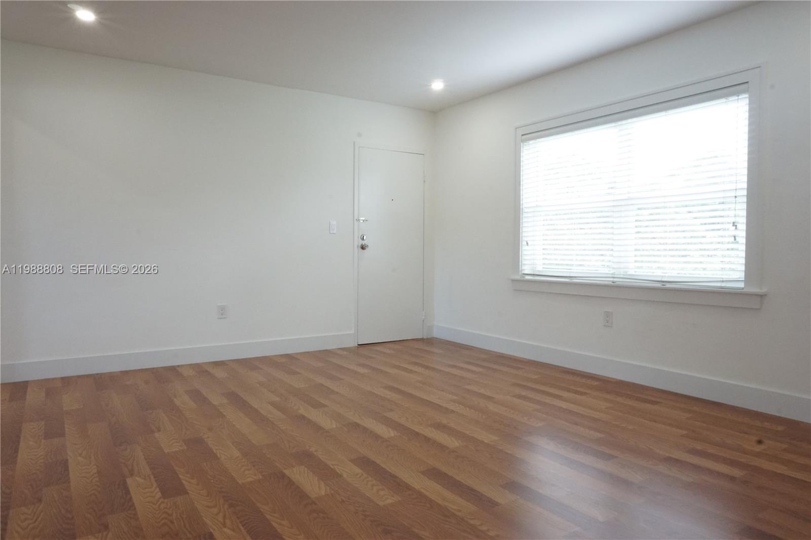 An empty room features white walls, wood-look flooring, a single window, and a white door — 7701 SW 55th Ave # C, Miami FL 33143, MIAMI, FL