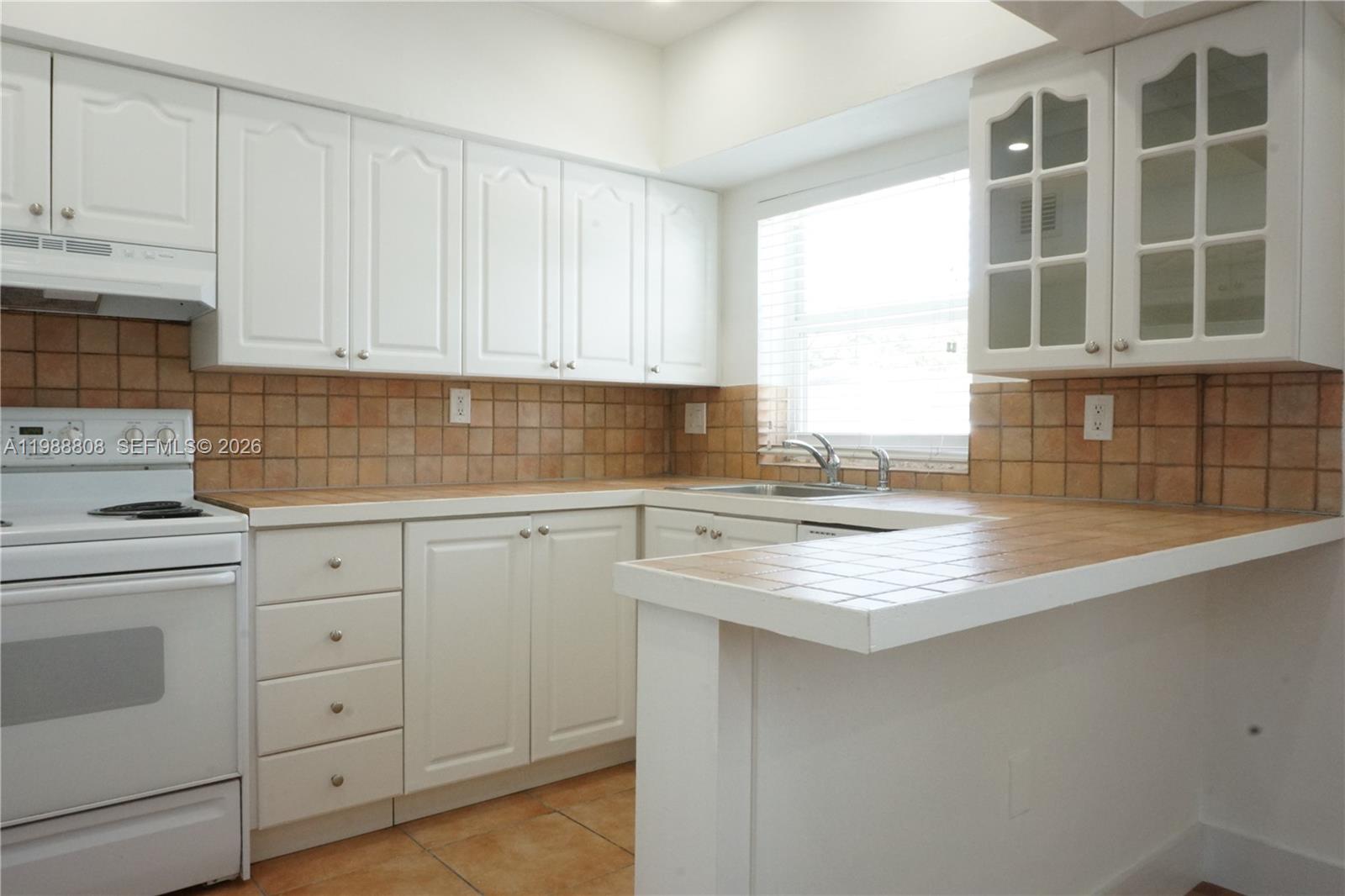 A kitchen features white cabinets, tiled countertops, a tiled backsplash, and a white stove — 7701 SW 55th Ave # C, Miami FL 33143, MIAMI, FL