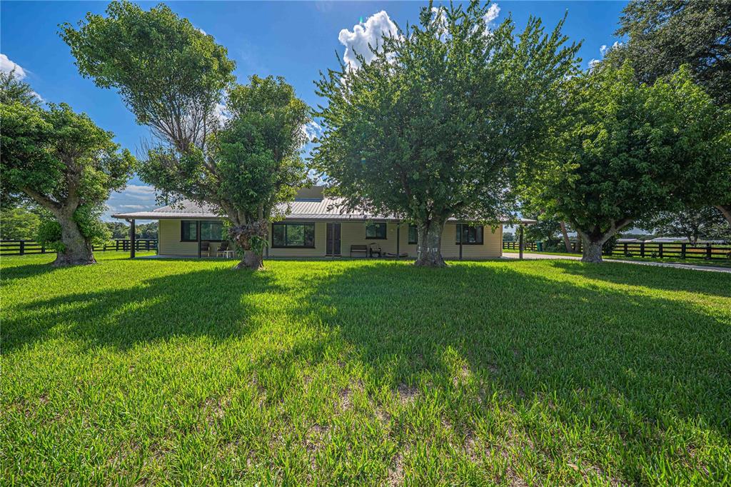 A single-story house with a metal roof sits behind large trees on a grassy lawn — 15111 NW 34TH TERRACE, OKEECHOBEE, FL