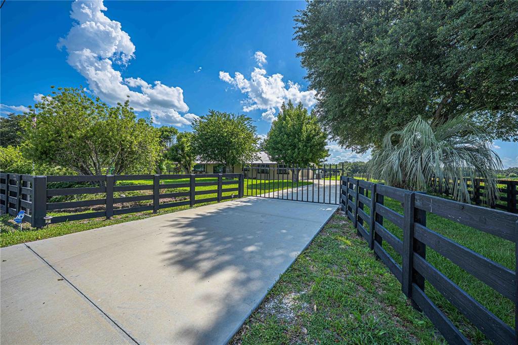 A concrete driveway leads through a black metal gate toward a house behind wooden fencing — 15111 NW 34TH TERRACE, OKEECHOBEE, FL