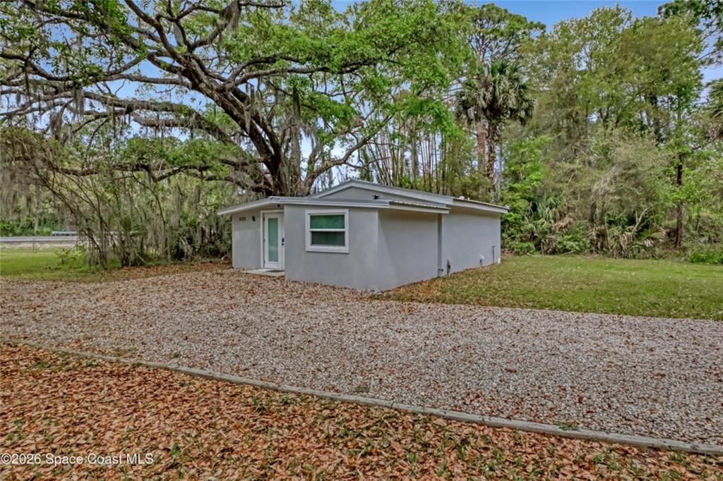 A small, light-gray house with a gravel driveway sits under a large oak tree — 4325 N HIGHWAY 1, MIMS, FL