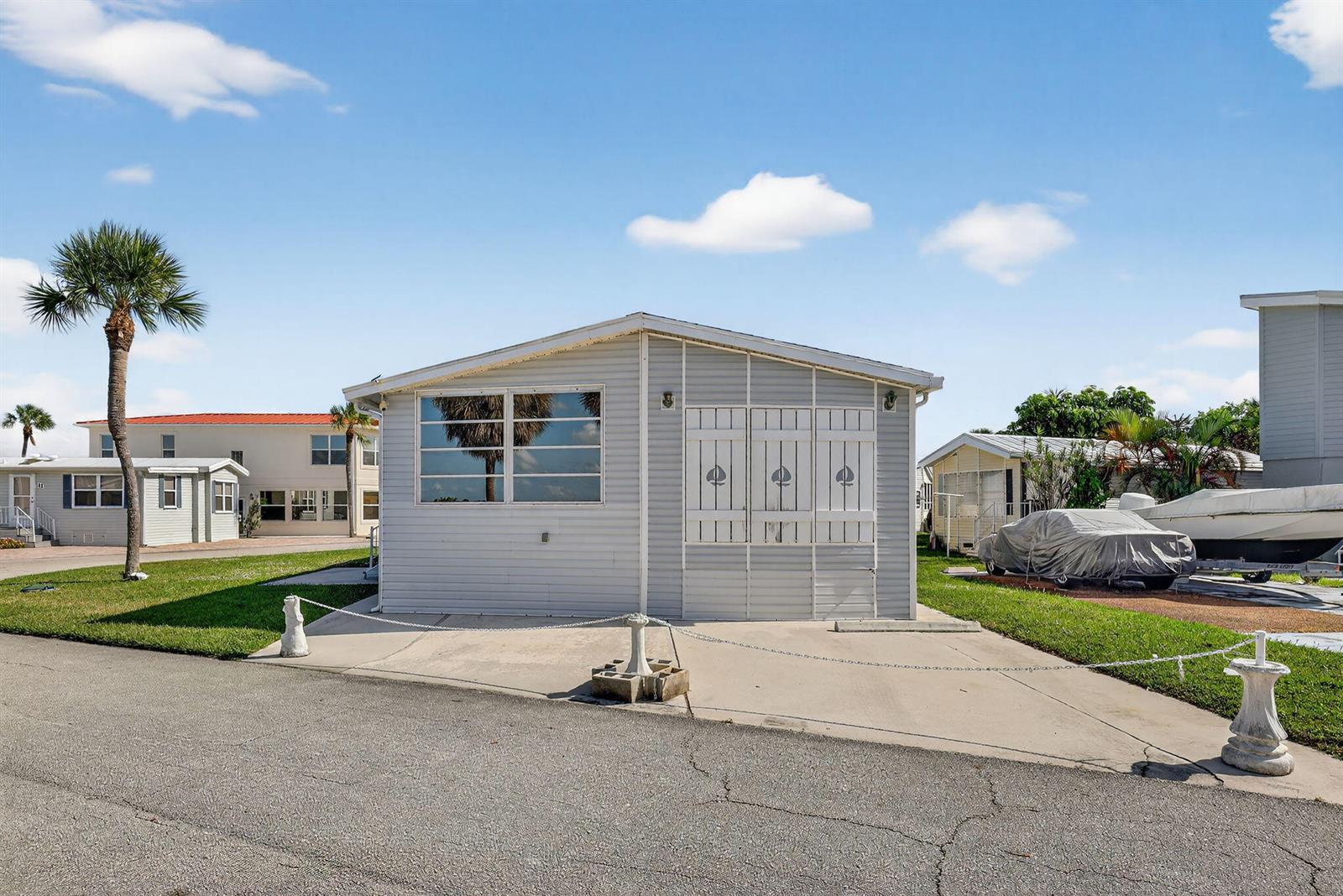 A light-colored mobile home with a concrete driveway and a chain barrier sits outdoors — 217 Nettles Boulevard, Jensen Beach FL 34957, JENSEN BEACH, FL