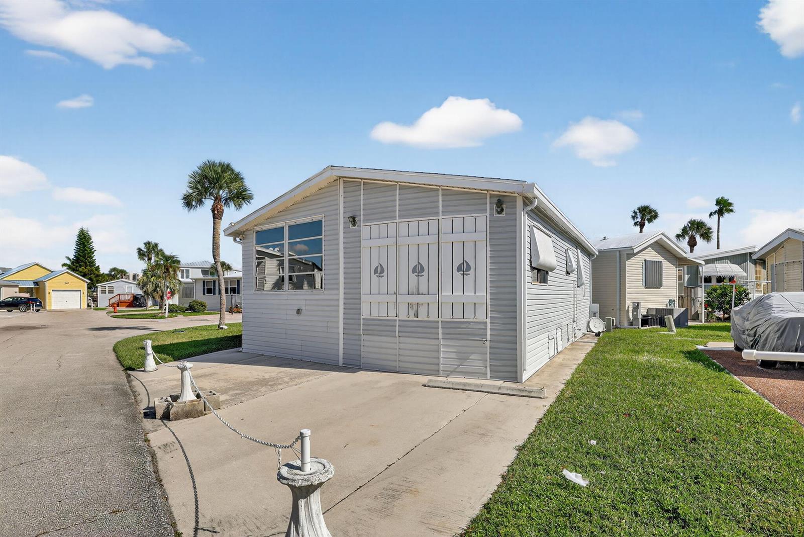 A light gray manufactured home features white shutters with sailboat cutouts and a concrete driveway — 217 Nettles Boulevard, Jensen Beach FL 34957, JENSEN BEACH, FL