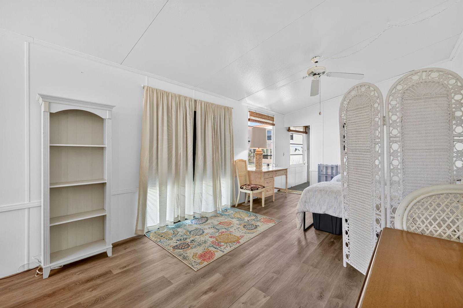 A bedroom features white walls, wood-look flooring, a ceiling fan, and a decorative room divider — 217 Nettles Boulevard, Jensen Beach FL 34957, JENSEN BEACH, FL