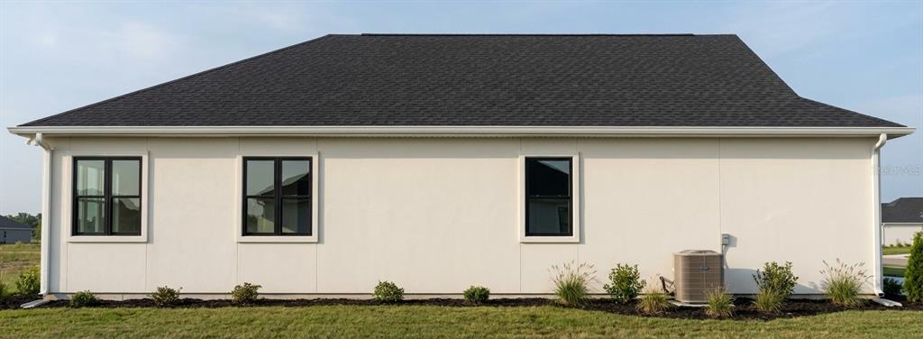 The exterior side view of a house features white stucco walls, black-framed windows, and landscaping — 4800 16TH AVENUE S, ST PETERSBURG, FL