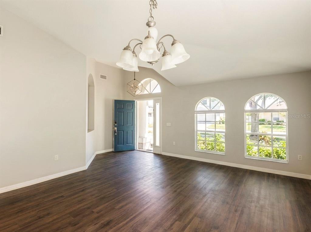 An empty living room features dark wood-look flooring, a chandelier, and arched windows — 210 SMOKEY HILL AVENUE, RUSKIN, FL