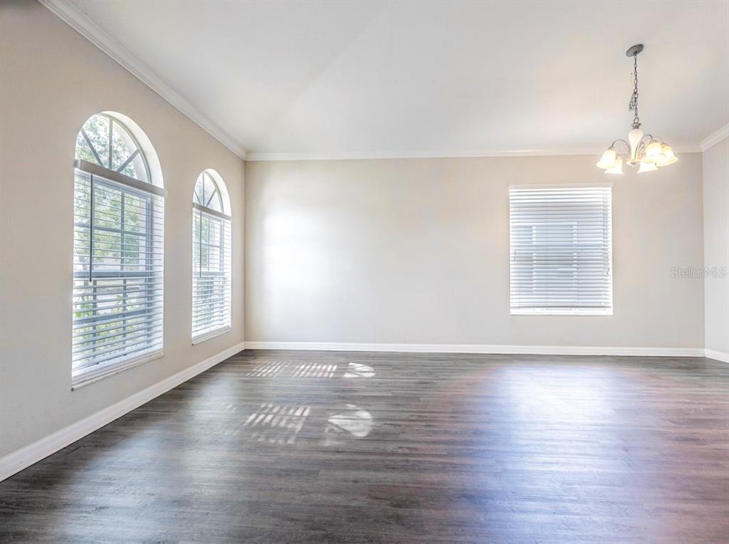 An empty room with dark wood-look flooring, light walls, arched windows, and a hanging chandelier — 210 SMOKEY HILL AVENUE, RUSKIN, FL