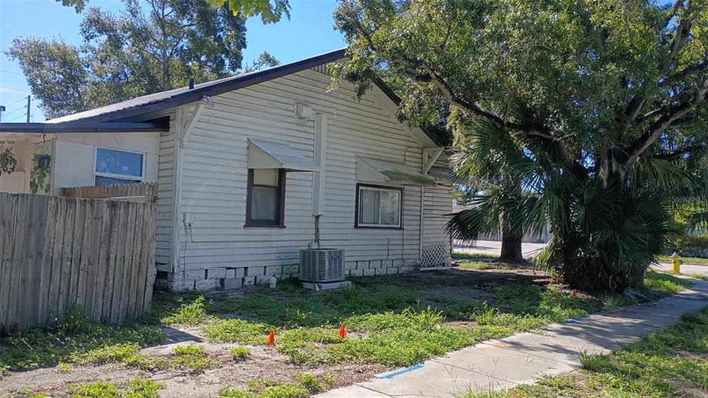 The exterior of a white, single-story house with a wooden fence and a large tree — 1623 7TH AVE N, ST PETERSBURG, FL