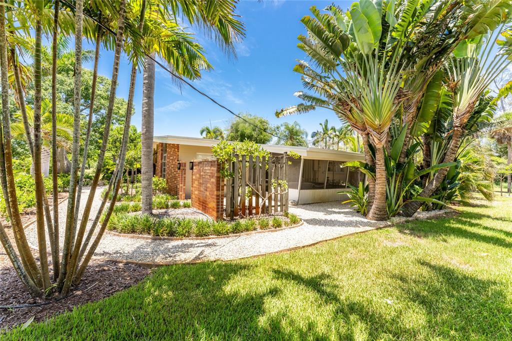 A brick house exterior features a screened-in porch, gravel landscaping, and lush tropical palm trees — 20 SPANIARDS ROAD, PLACIDA, FL