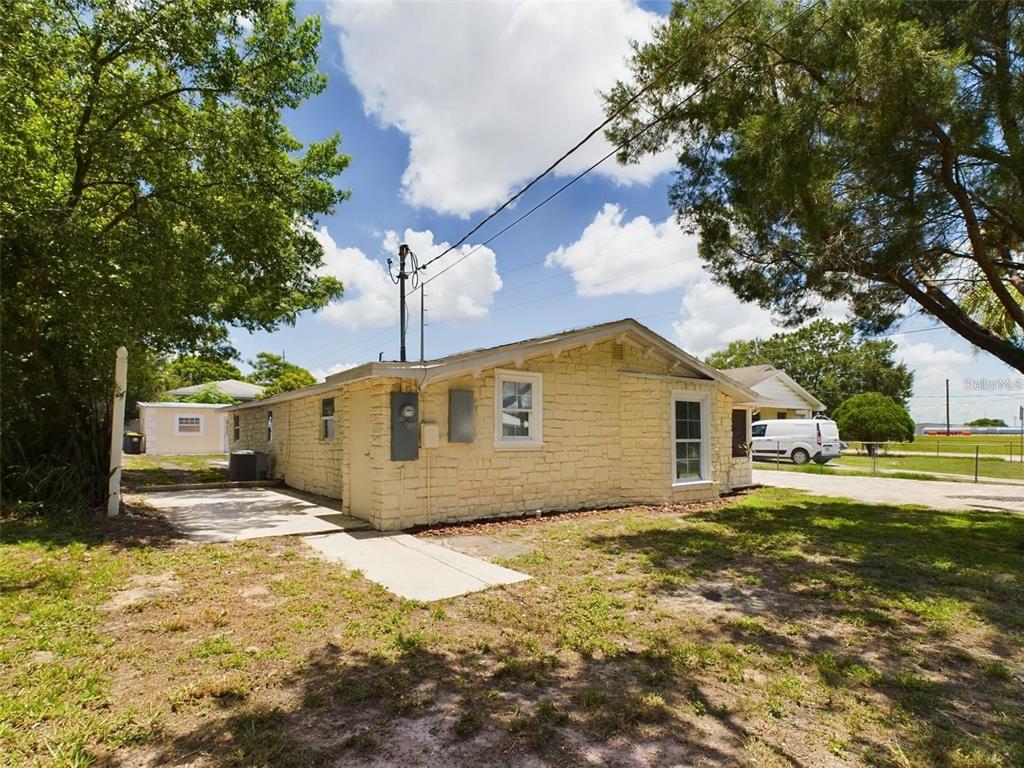 A side view of a yellow stone-clad house with a concrete walkway and utility meters — 617 LIME, AUBURNDALE, FL