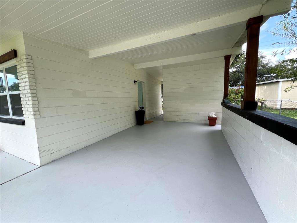 A covered concrete patio features white horizontal siding, a dark wooden post, and a doorway — 2004 E BROAD STREET, TAMPA, FL