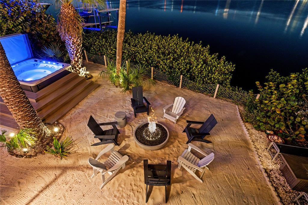 A sandy backyard patio features a fire pit, Adirondack chairs, and a hot tub at night — 151 PUNTA VISTA DRIVE, ST PETE BEACH, FL