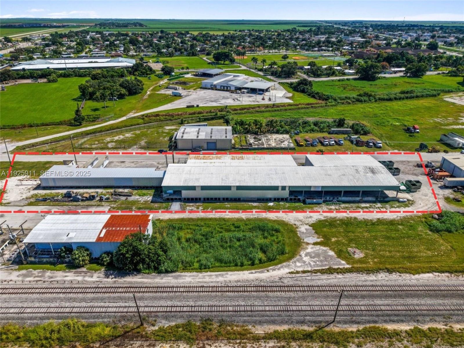 An aerial view shows a large industrial warehouse building outlined in red near railroad tracks — 901 NW 9th St, Belle Glade FL 33430, BELLE GLADE, FL