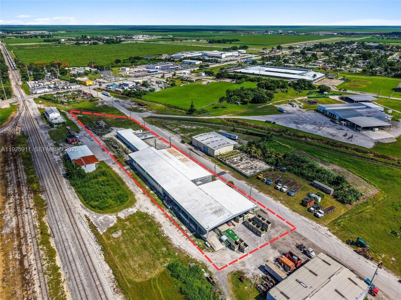 An aerial view shows a long industrial warehouse building outlined in red near railroad tracks — 901 NW 9th St, Belle Glade FL 33430, BELLE GLADE, FL
