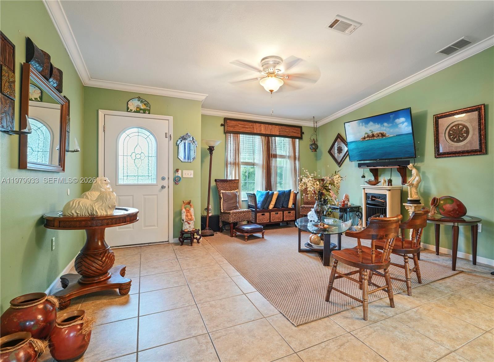 A living room with green walls, tile flooring, a ceiling fan, and a mounted television — 3713 Wild Violet Avenue, Sebring FL 33876, SEBRING, FL