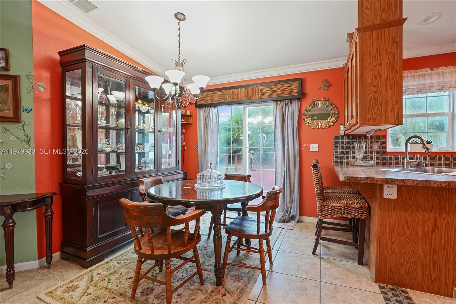 A dining area with a round wooden table, hutch, and kitchen counter on orange walls — 3713 Wild Violet Avenue, Sebring FL 33876, SEBRING, FL