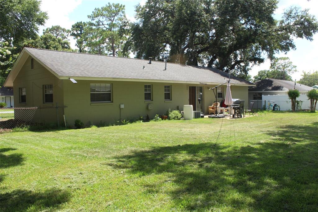 The exterior of a single-story house with a grassy backyard and large shade trees — 5705 SE 2ND STREET, OCALA, FL