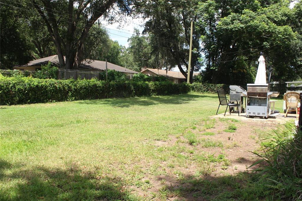 A grassy backyard features a patio area with a grill, outdoor furniture, and a fence — 5705 SE 2ND STREET, OCALA, FL