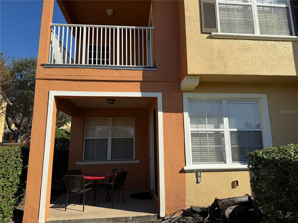 A ground-level patio with a table and chairs sits beneath a second-story balcony — 860 ASSEMBLY COURT, REUNION, FL