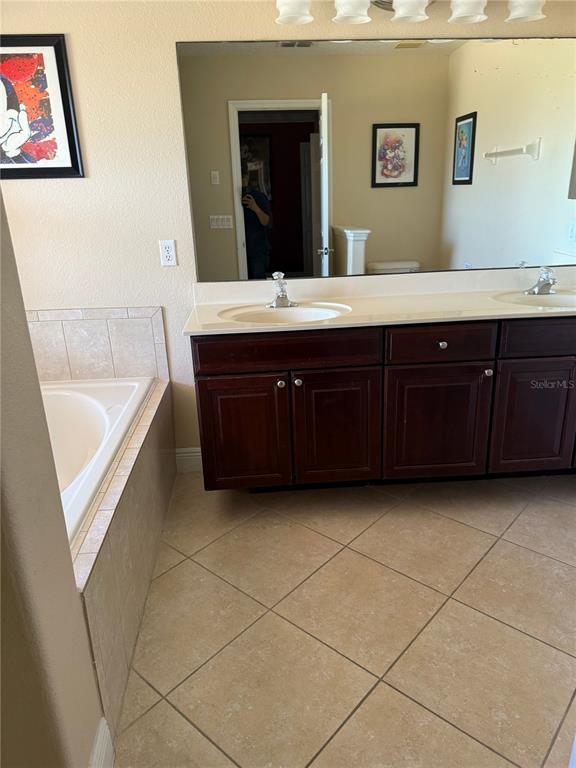 A bathroom features a double vanity with dark cabinets, a large mirror, and a bathtub — 860 ASSEMBLY COURT, REUNION, FL