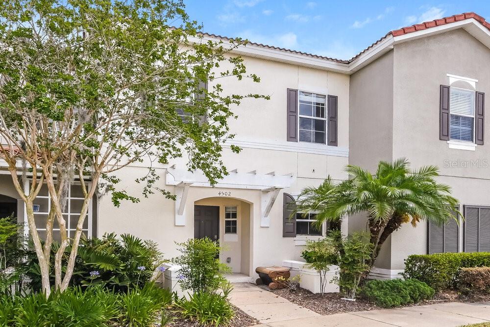 A two-story townhouse exterior features a beige stucco facade, dark shutters, and a small pergola — 4502 ALBERTO CIRCLE, KISSIMMEE, FL