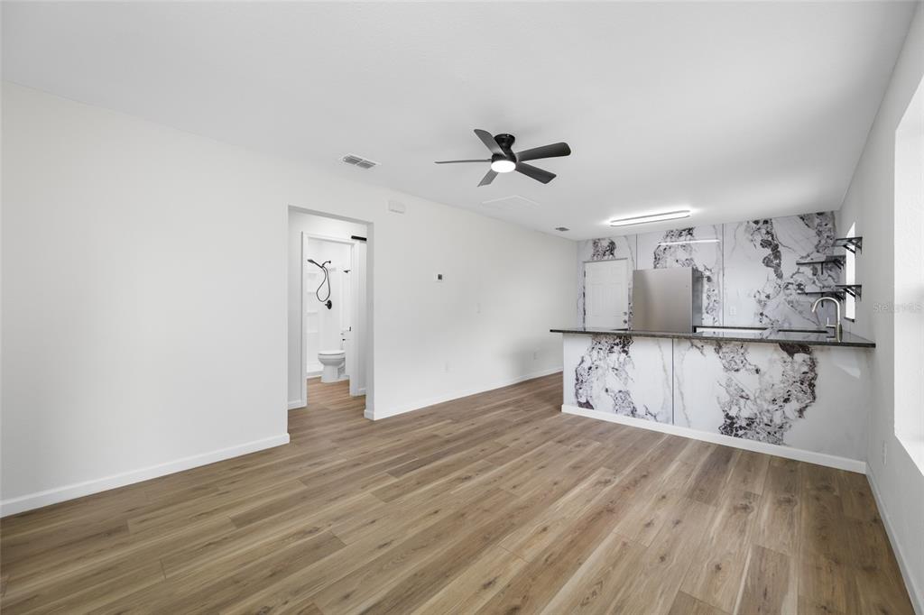 A room with wood-look flooring, a ceiling fan, and a kitchen featuring marble-patterned cabinetry — 308 W 10TH STREET, LAKELAND, FL