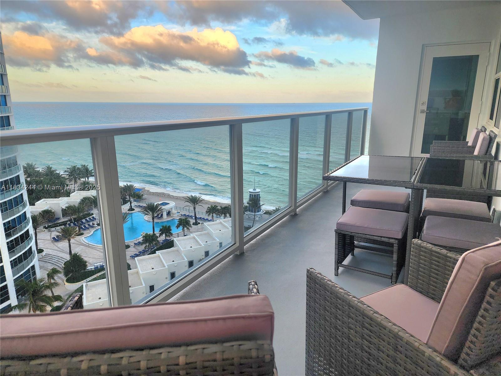 A balcony with wicker furniture overlooks a swimming pool and the ocean — 3505 S Ocean Dr # 1409, Hollywood FL 33019, HOLLYWOOD, FL