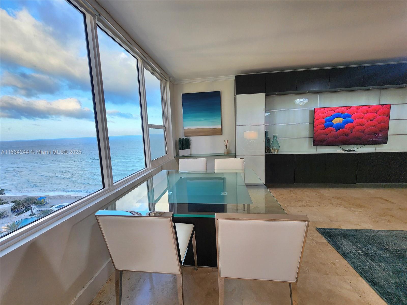 A dining area features a glass table, modern chairs, and floor-to-ceiling windows overlooking the ocean — 3505 S Ocean Dr # 1409, Hollywood FL 33019, HOLLYWOOD, FL
