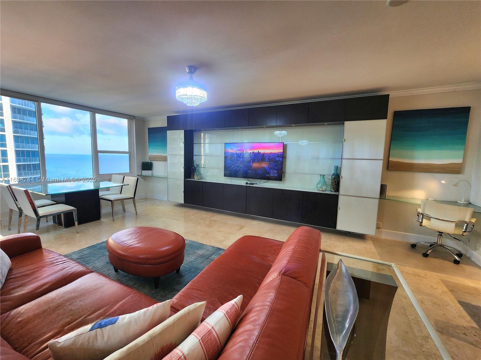 A living room features a large red sofa, a media wall, and floor-to-ceiling ocean views — 3505 S Ocean Dr # 1409, Hollywood FL 33019, HOLLYWOOD, FL