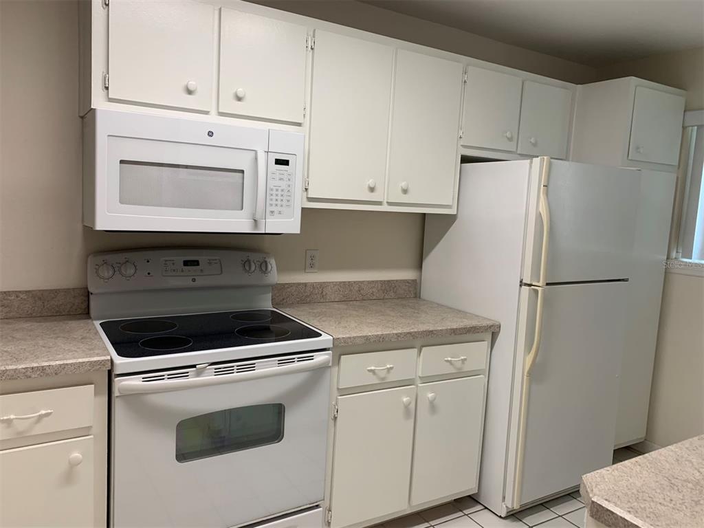 A kitchen features white cabinets, a white microwave, a white electric stove, and a refrigerator — 150 HARBORSIDE AVENUE UNIT 229, PUNTA GORDA, FL