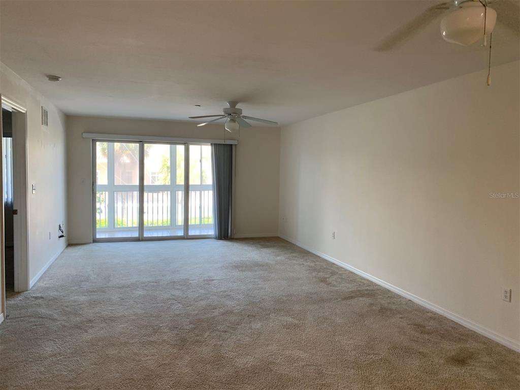 A spacious living room features beige carpeting, a ceiling fan, and sliding glass balcony doors — 150 HARBORSIDE AVENUE UNIT 229, PUNTA GORDA, FL