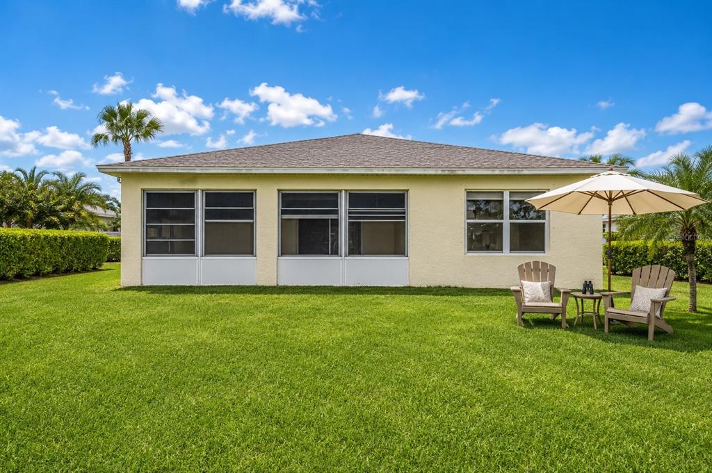 The back exterior of a yellow house features a screened-in porch and two patio chairs — 57 HUARTE WAY, PORT ST LUCIE, FL