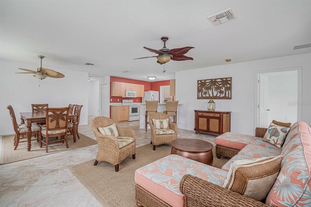 An open-concept living and dining area features wicker furniture, tile flooring, and a kitchen — 57 HUARTE WAY, PORT ST LUCIE, FL