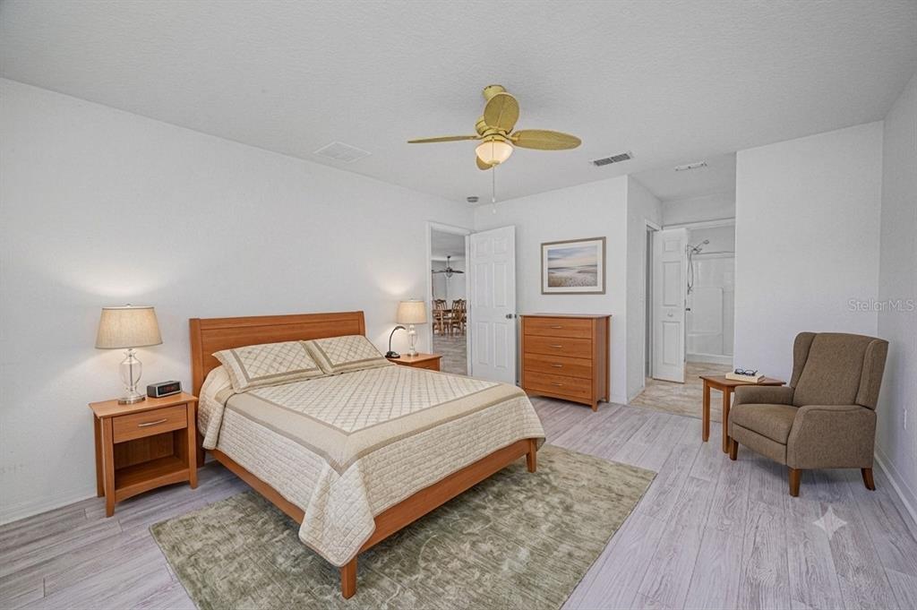 A bedroom features a wooden bed, a matching dresser, a beige armchair, and light flooring — 57 HUARTE WAY, PORT ST LUCIE, FL