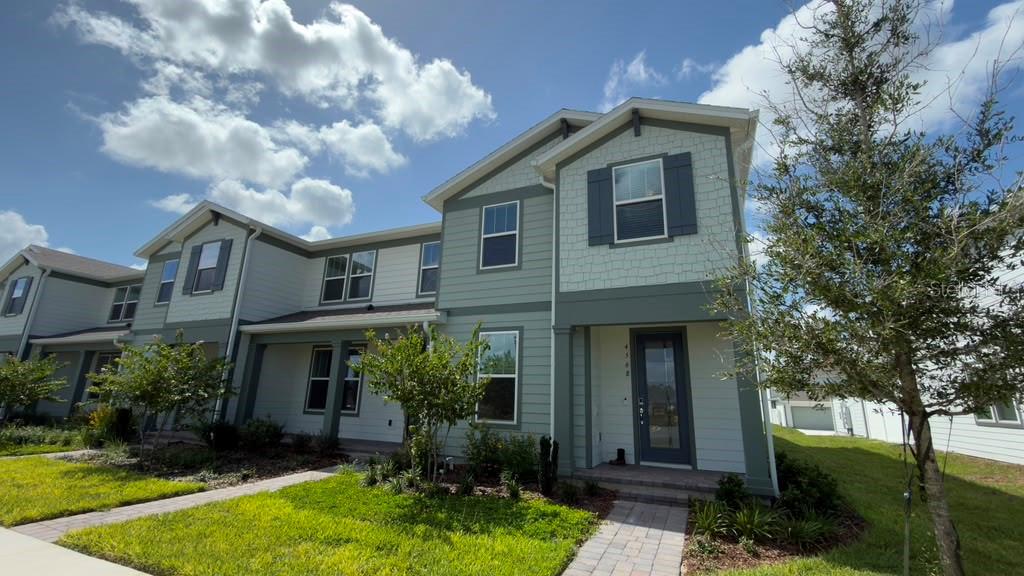 A two-story townhouse with light green siding, dark shutters, and a paved walkway — 4568 ORCHARD VIEW ALLEY, CLERMONT, FL