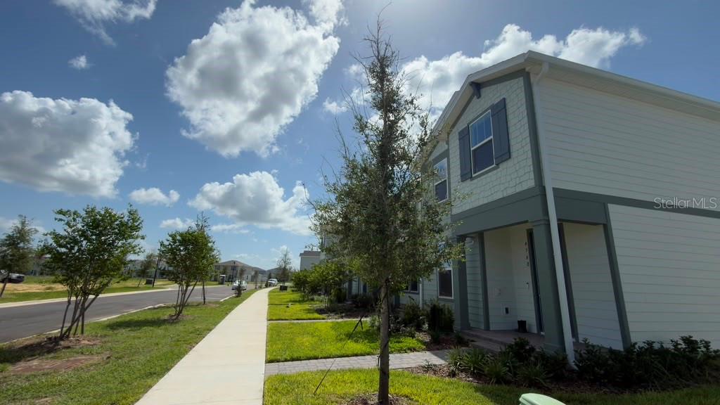 A two-story townhouse exterior with light siding, a covered entryway, and a sidewalk — 4568 ORCHARD VIEW ALLEY, CLERMONT, FL