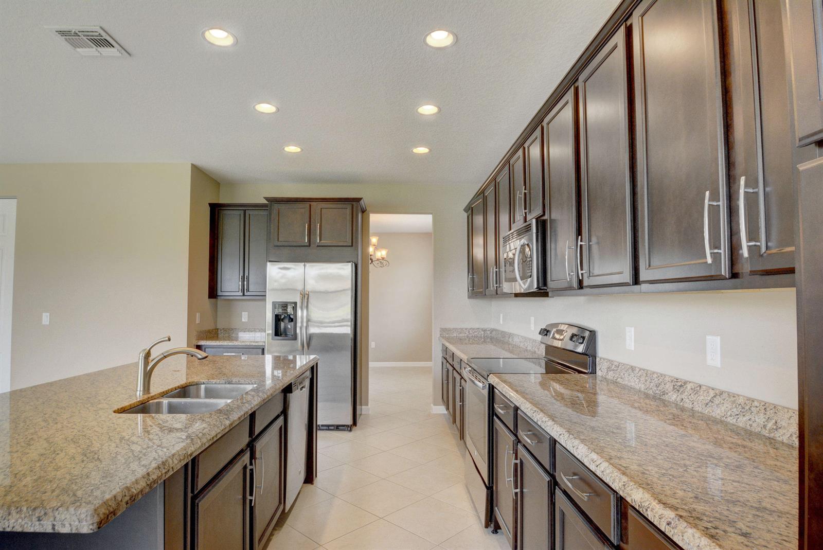A kitchen features dark wood cabinets, granite countertops, stainless steel appliances, and a central island — 2916 Payson Way, Wellington FL 33414, WELLINGTON, FL