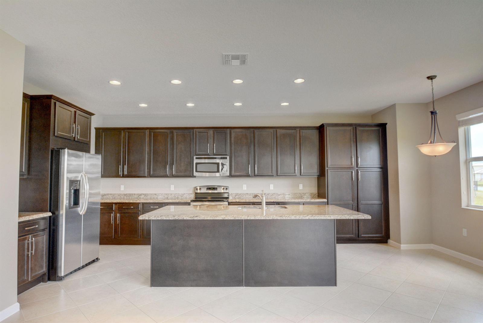 A kitchen features dark wood cabinetry, granite countertops, a central island, and stainless steel appliances — 2916 Payson Way, Wellington FL 33414, WELLINGTON, FL