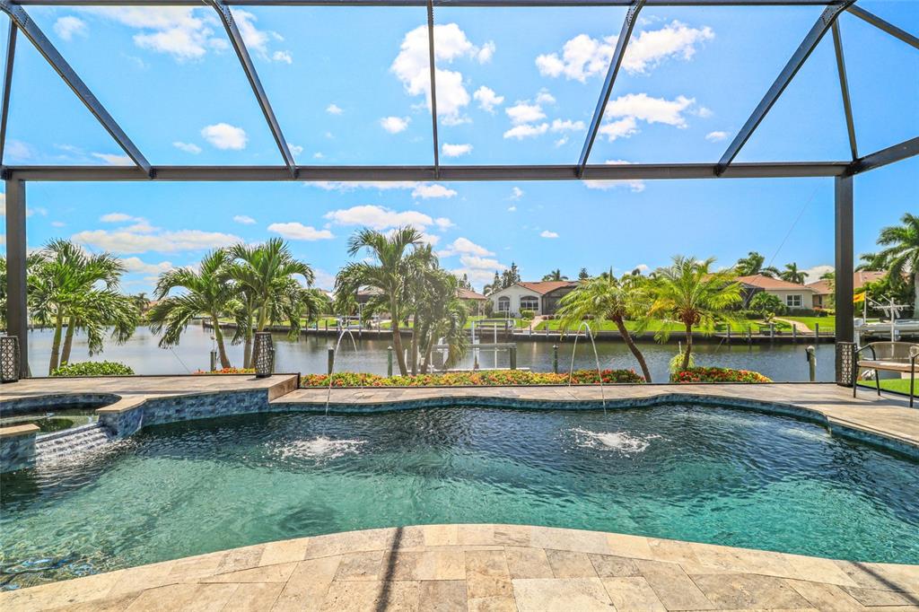 A screened-in pool patio overlooks a canal with palm trees and houses in the background — 1317 PINE SISKIN DRIVE, PUNTA GORDA, FL