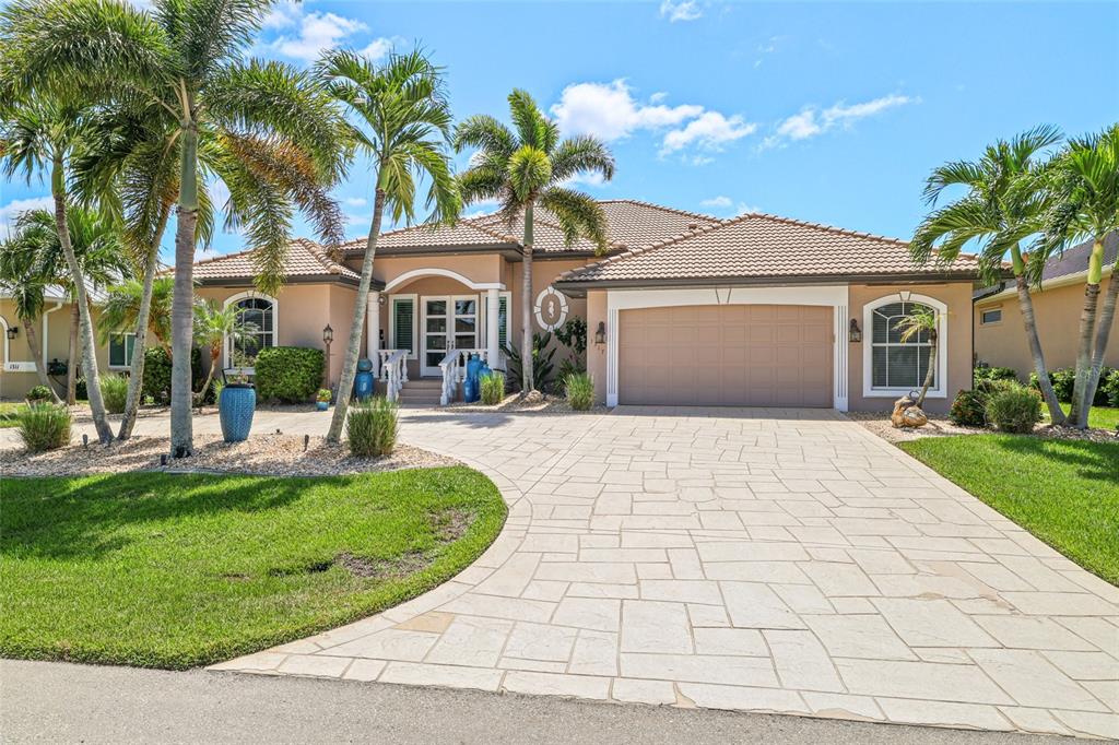 A single-story house with a tan exterior, tile roof, paved driveway, and several palm trees — 1317 PINE SISKIN DRIVE, PUNTA GORDA, FL